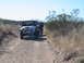 1996 Ford Bronco - People are gathered around the front of a Jeep Wrangler on a dusty trail, with another vehicle behind.