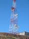 1996 Ford Bronco - A tall radio tower stands against a bright blue sky, with a building visible near its foundation.