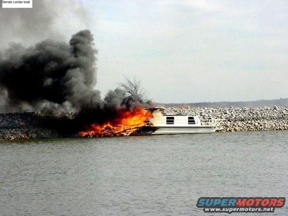 Houseboat engulfed in flames and smoke, docked near a rocky shore