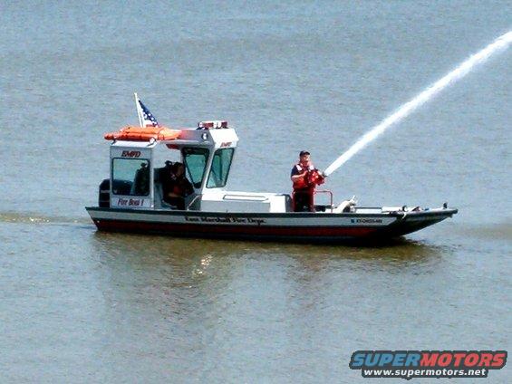 Fire boat with a person operating a water cannon, spraying water. Text on boat reads 'Knox Marshall Fire Dept.'