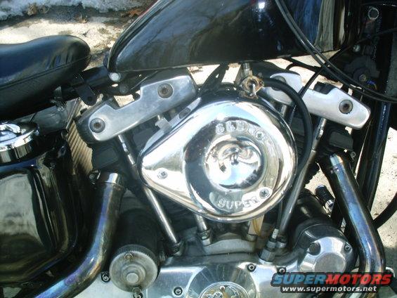Close-up of a chrome air cleaner cover on a motorcycle engine, with 'SUPER' visible