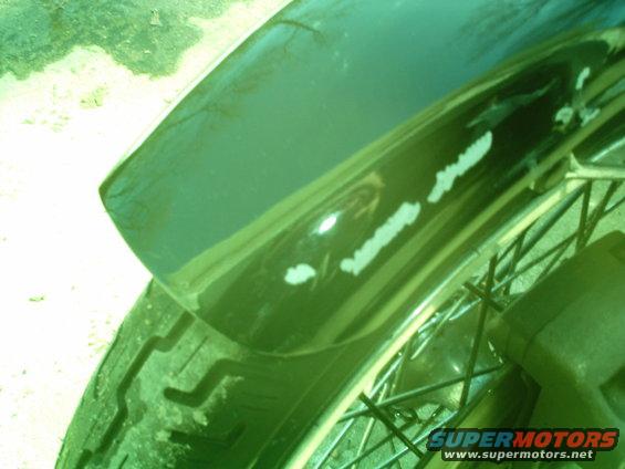 Green motorcycle fender with white scuffs over a spoked wheel and tire