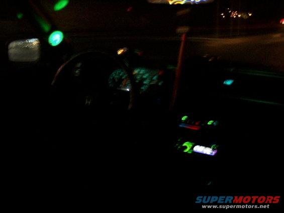 Car interior at night, dashboard lights and radio display illuminated, green lights on ceiling