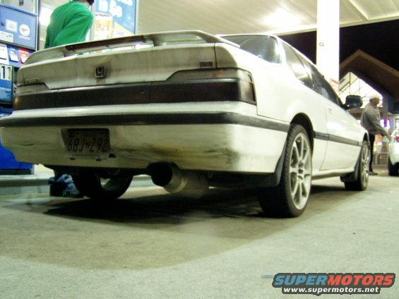 White coupe with a spoiler and aftermarket exhaust, viewed from the rear