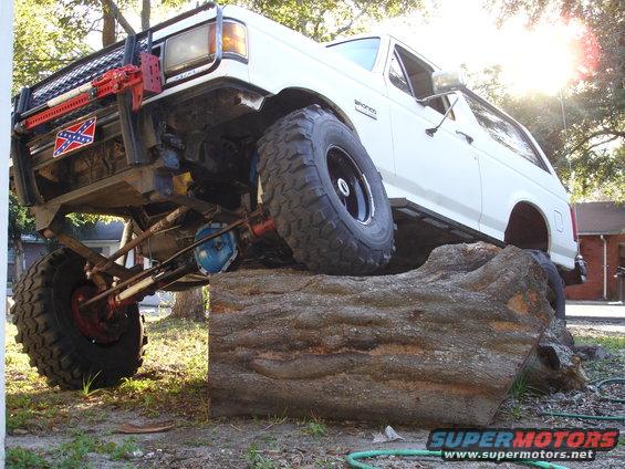 1989 Ford Bronco with lifted suspension and large tires on a log