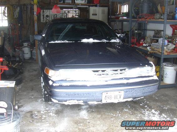 Dark sedan with snow on windshield and bumper, parked in a garage