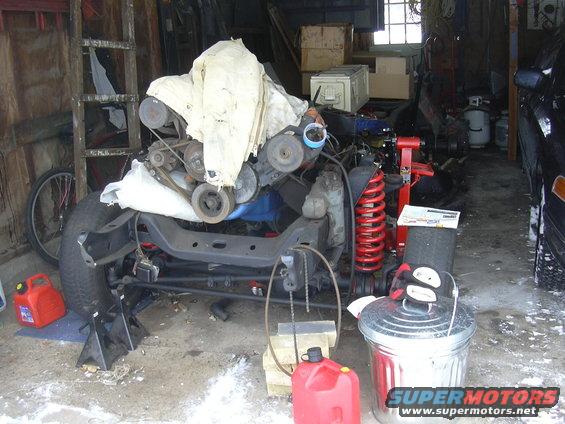 Engine and chassis parts covered in a white tarp, with red springs and a tire visible