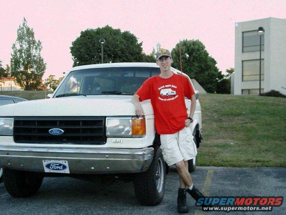 guy in red shirt and shorts leaning on front of white Ford F-series truck