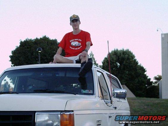 1988 Ford Bronco with a person sitting on the roof, wearing a red t-shirt with a graphic