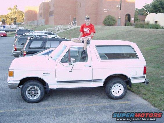 guy sitting on roof of white Ford Bronco, parked next to other vehicles