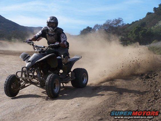 Dark quad bike kicking up dust on a dirt track, rider wearing protective gear