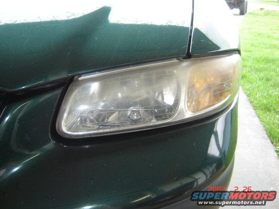 Close-up of a green minivan's driver side headlight assembly. The lens is cloudy and yellowed