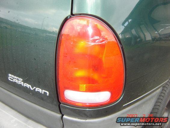 Close-up of a green Grand Caravan's damaged tail light. Text on the vehicle reads 'GRAND CARAVAN'