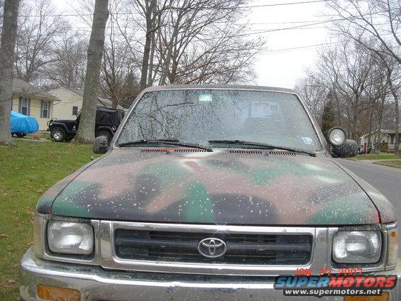 Camouflaged Toyota pickup truck front view, showing grille with Toyota logo, headlights, and windshield