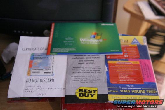 Stack of computer software boxes including Windows Home Edition and Best Buy flyers