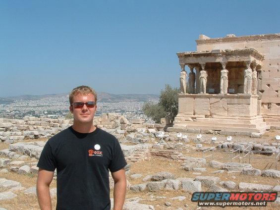 Man in black t-shirt and sunglasses at ancient ruins with city in background