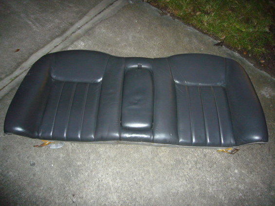 Black leather car rear seat with center armrest, resting on concrete