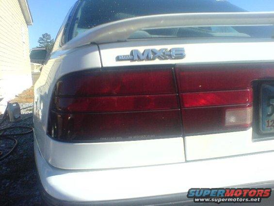 Rear of a white Mazda MX-6 with a spoiler. Shows taillights and part of a license plate