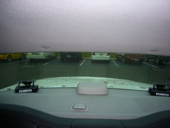 Interior view from a car's rear seat, looking out at parked cars. A radar detector is visible on the rear deck