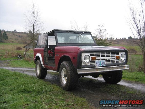 1968 Ford Bronco with soft top, red body, black top, parked on a dirt road