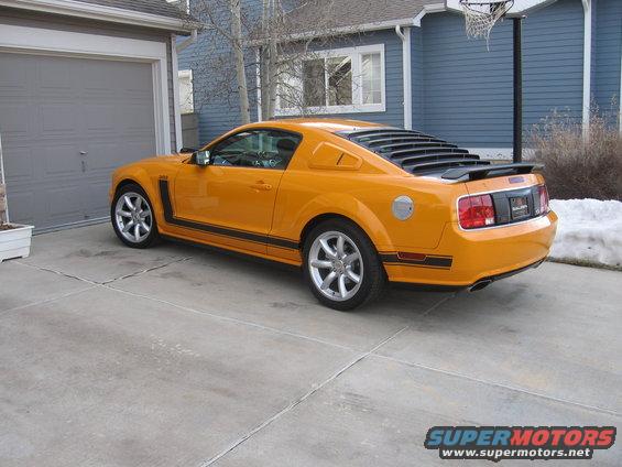 Orange Ford Mustang with black stripes and louvers on the rear window, parked in a driveway