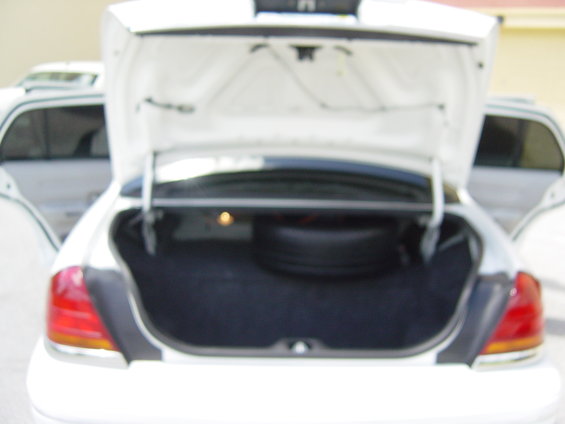 2000 Ford Crown Victoria trunk open, showing spare tire and interior. Another white car is visible to the left