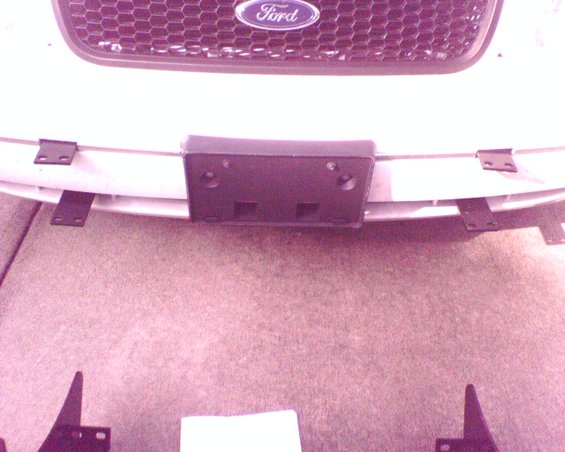 Front of a Ford vehicle showing the grille with the Ford logo and a license plate bracket attached to the bumper