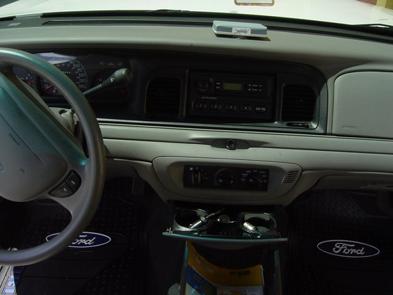 2000 Ford Crown Victoria interior dashboard with steering wheel, radio, and climate controls visible. Ford floor mats are on the driver and passenger sides