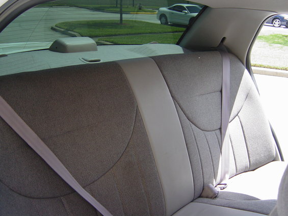 Back seat and shoulder belts inside a car. Another car is visible through the rear window