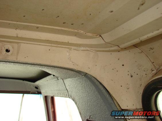 Interior view of a vehicle's ceiling and upper window frame, showing textured gray trim and beige headliner with some cracks