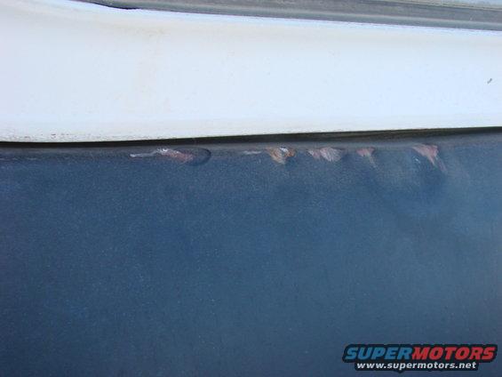 Rust spots on dark blue vehicle panel below white trim