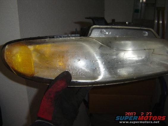 Someone is holding a car headlight assembly. It looks dirty and has water spots