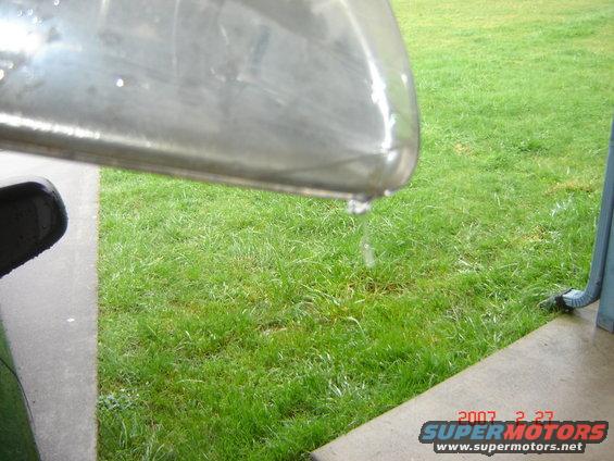 Water drips off a shiny metal object, with grass and a concrete path visible