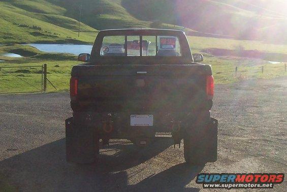 Dark pickup truck rear view, lifted suspension, large tires, tow hitch, and a 'For Sale' sign in the rear window