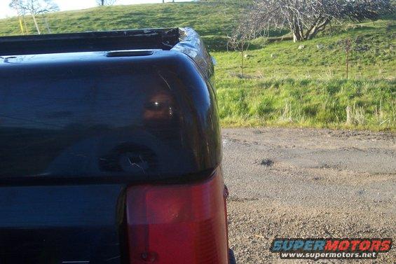 Black pickup truck rear corner, showing taillight and bed rail. The truck appears to be from the early to mid-1990s