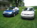 2005 Ford Focus - Two Ford Focus sedans are parked on a lawn in front of a house with a cornfield in the background.
