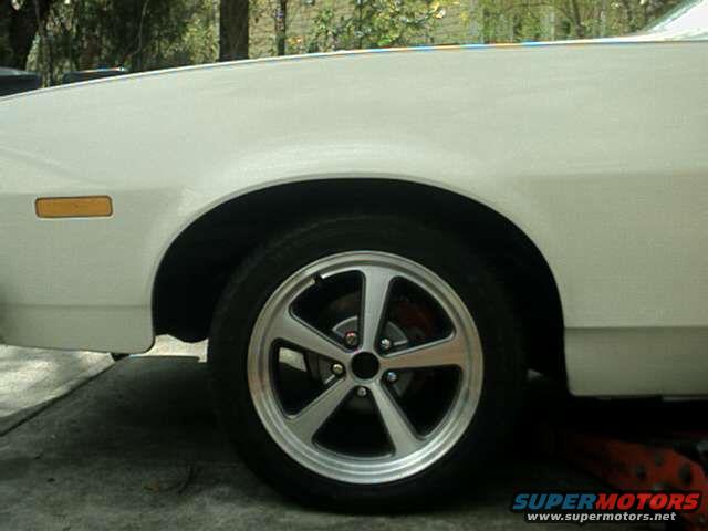 White car fender and wheel with five-spoke alloy rim, amber turn signal, and red brake caliper