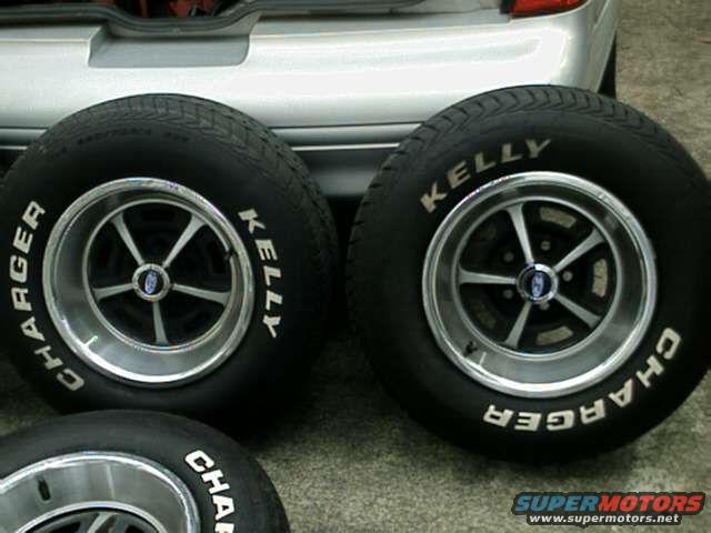 Two tires with 'Charger' and 'Kelly' text on them, mounted on classic five-spoke wheels