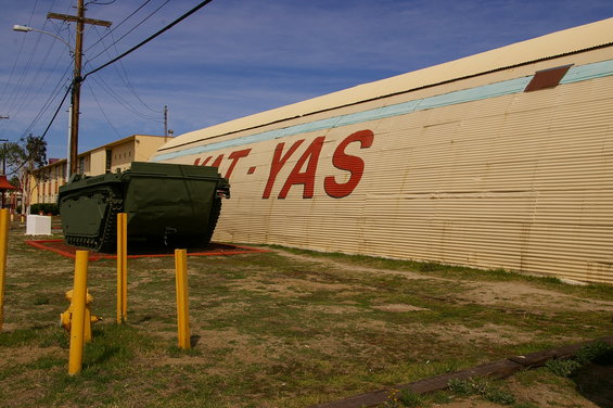 Green amphibious tracked vehicle parked on display in front of a corrugated metal building with red lettering