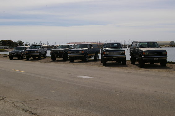 Several Ford Bronco SUVs and pickup trucks parked by the water