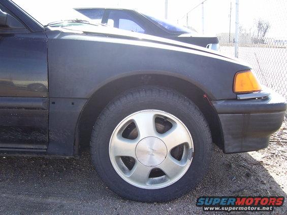 Car's front fender, wheel, and part of bumper. Another car is visible behind it