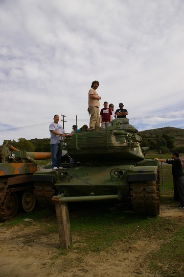 Green tanks with people standing on them under a cloudy sky