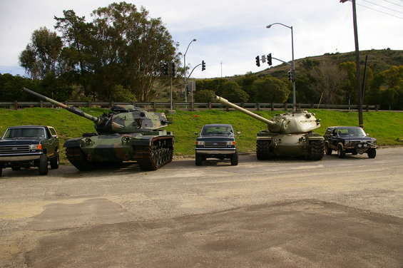 two tanks and three trucks parked on pavement
