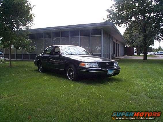 Black 1998 Ford Crown Victoria parked on grass in front of a building