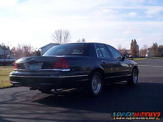 Dark 1998 Ford Crown Victoria sedan, rear 3/4 view, parked on asphalt with a grassy area to the left