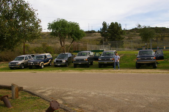 Dark blue Ford Bronco with a white camper shell, parked in a line with other vehicles