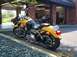 1998 Ford Crown Victoria - A yellow motorcycle is parked outside a garage, with a brown car visible inside.