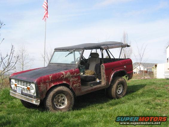 Red 1968 Ford Bronco with soft top and removed driver's door, covered in mud