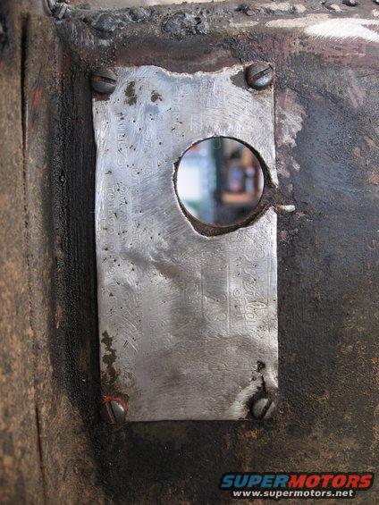 Close-up of a riveted metal plate with a hole in it, attached to a rough surface