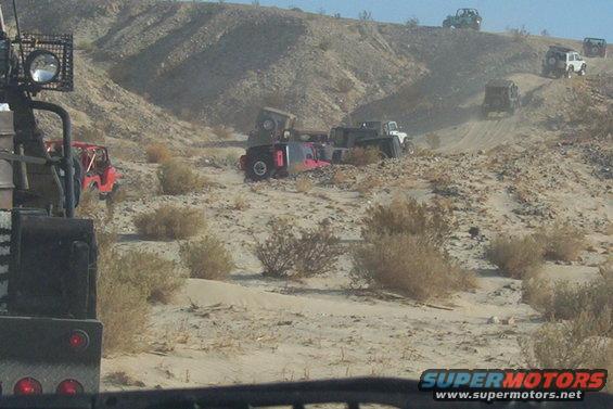 Several off-road vehicles driving and one overturned in a dusty desert